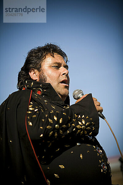 Elvis impersonator in a black costume sings for the crowd.