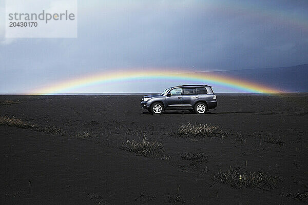 Four wheel dive car in the ash fall from volcano EyjafjallajÃ¶kull  with a perfect rainbow in the background