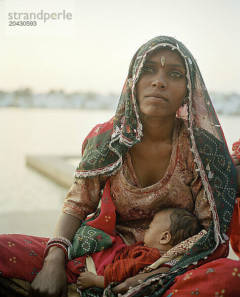 A mother and child sit beside sacred Pushkar Lake as the sun sets.