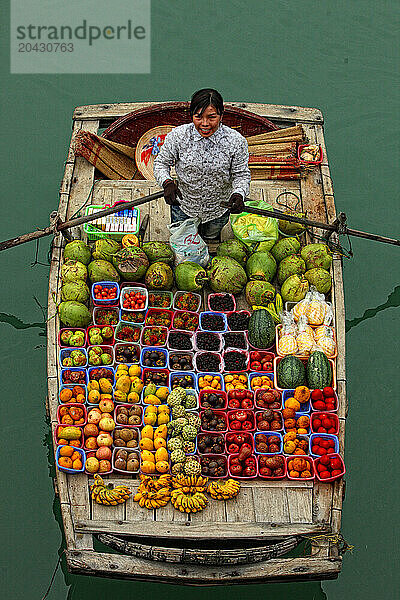 fruit seller paddles boxes of fruit in a boat on Halong Bay.