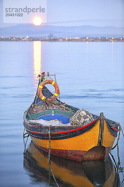 Traditional moliceiro rowboat in front of sun setting over coastal city