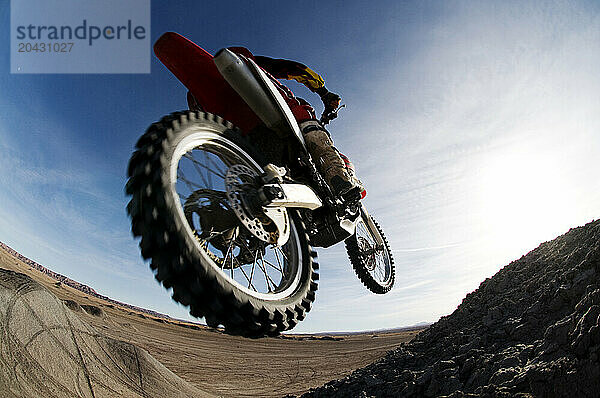 A young man jumps his dirt bike high in the air while motocross riding the surreal dunes near Cameron  AZ.