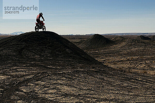 A young man rides his dirt bike up and over a hill while motocross riding the surreal dunes near Cameron  AZ.