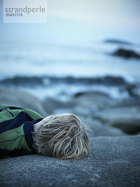 boy lies on rock on maine coast