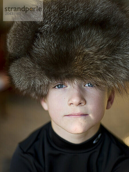 boy in big fur hat stares at camera