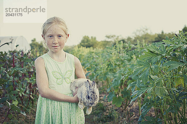 Girl holding a rabbit in a filed of okra