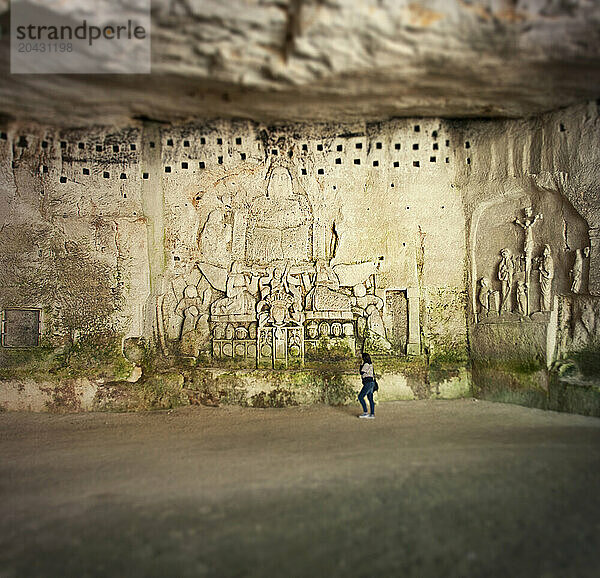 Woman walking in front of stone carving of Last Judgement within the old Addey in Brantome.