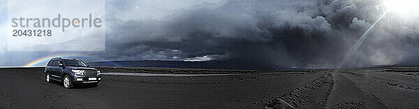 Panorama of a four wheel dive car in the ash fall from volcano EyjafjallajÃ¶kull  with a perfect rainbow in the background