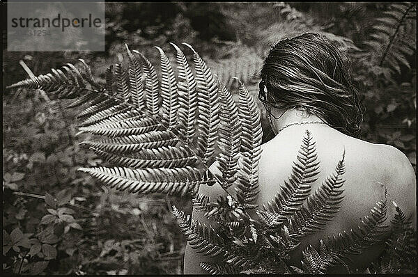 A young women looking away from the camera holds a fern frond behind her back in the thick forest surrounding Lake Taupo  North