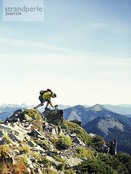 A hiker on a mountain top builds a rock cairn.