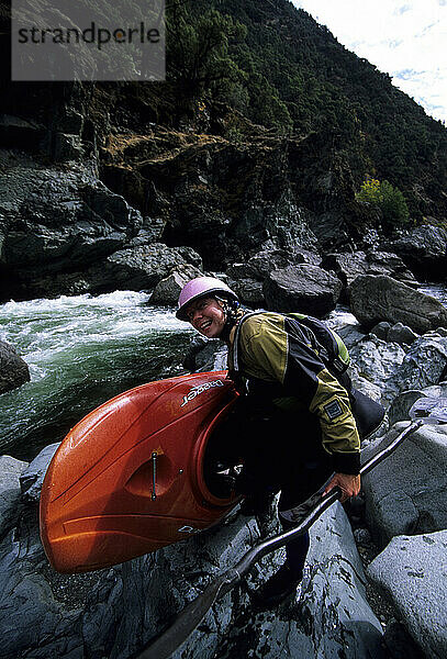 A smiling woman kayaker lifts her boat next to a rapid in the Burnt Ranch Gorge  Trinity River  California.