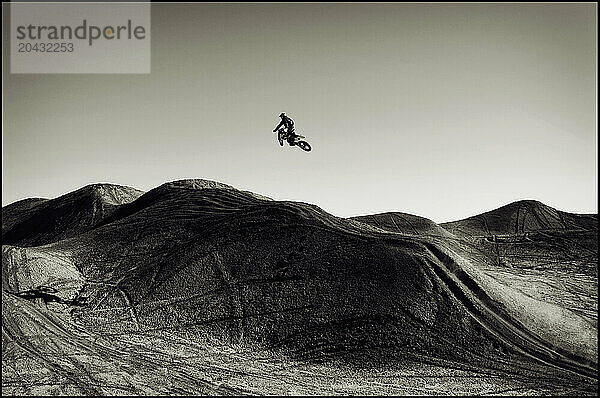 A young man jumps his dirt bike high in the air while motocross riding the surreal dunes near Cameron  AZ.