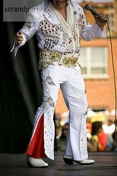 Elvis impersonator holding a microphone on stage performing in front of a crowd.