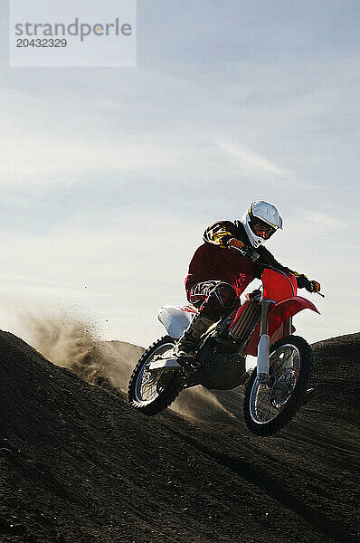 Dust and dirt fly as a young man banks his dirt bike into a hard turn while motocross riding on the surreal dunes near Cameron  AZ.