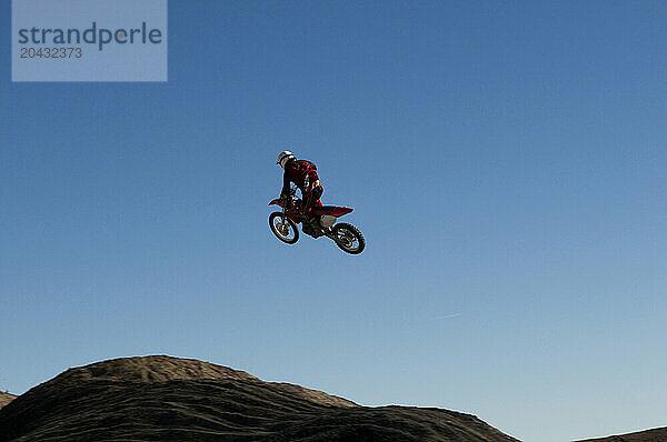 A young man jumps his dirt bike high in the air while motocross riding the surreal dunes near Cameron  AZ.