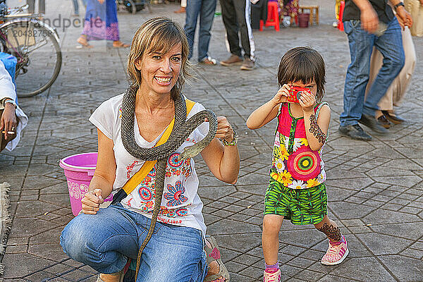 A Tourist Holding A Snake In Jemaa El Fna Square In Marrakech While Her Daughter Takes A Photo