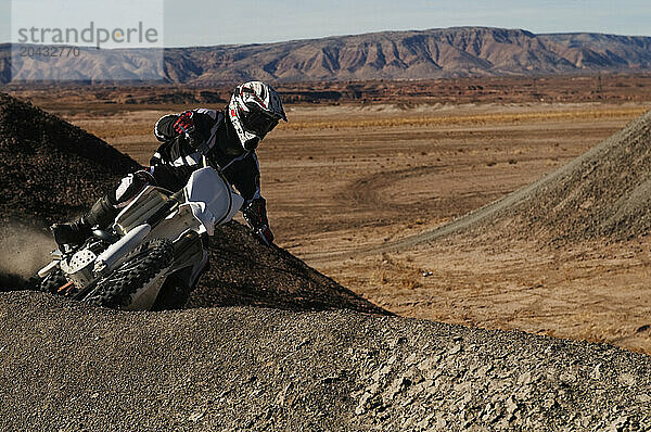 Dust and dirt fly as a young man banks his dirt bike into a hard turn while motocross riding on the surreal dunes near Cameron  AZ.