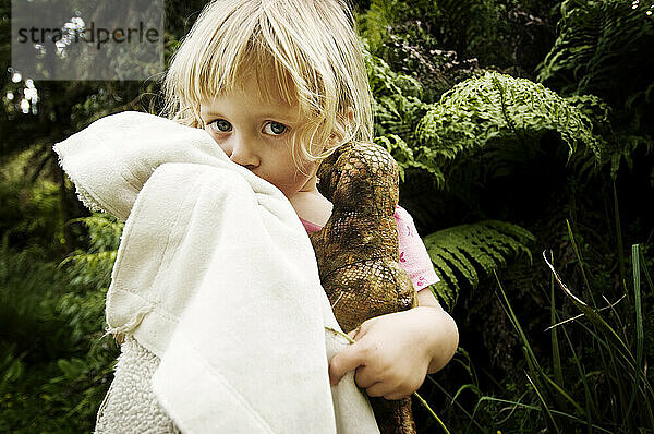 A young girl snuggles her blanket and stuffed dinosaur while hiking in the Waitomo Region of New Zealand.