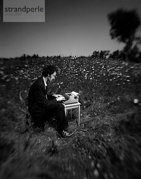 Black & White Selective focus portrait of handsome young man on a type writer in a field