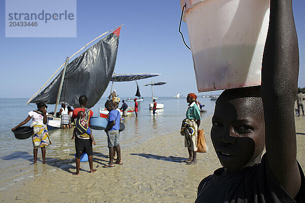 People carrying bowls and buckets in front of sailboats waiting on coastal beach  Mozambique