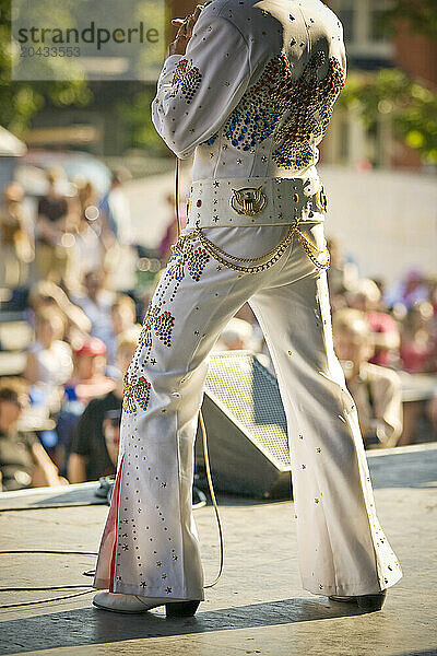 Elvis impersonator holding a microphone on stage performing in front of a crowd.