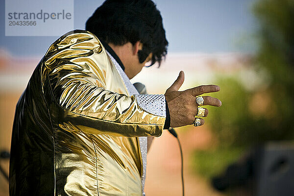 Elvis impersonator holding a microphone on stage performing in front of a crowd.