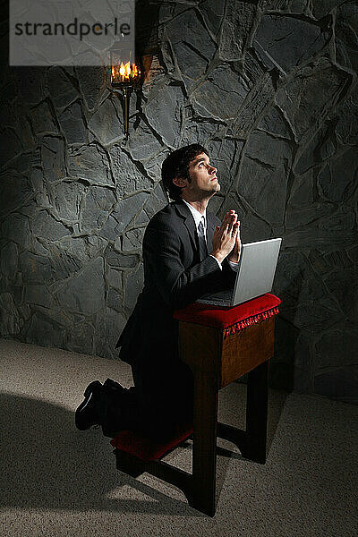 Businessman praying with laptop computer