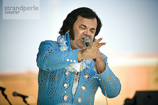 Elvis impersonator in a blue costume sings for the crowd.