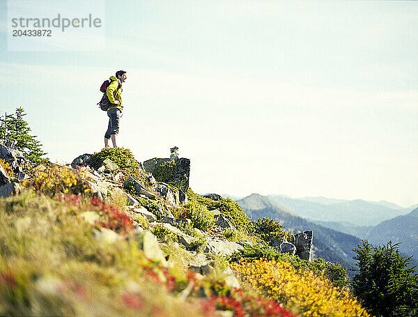 A male hiker on a mountain top looks off into the distance.