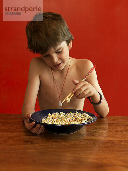 A boy eats cereal with chopsticks.