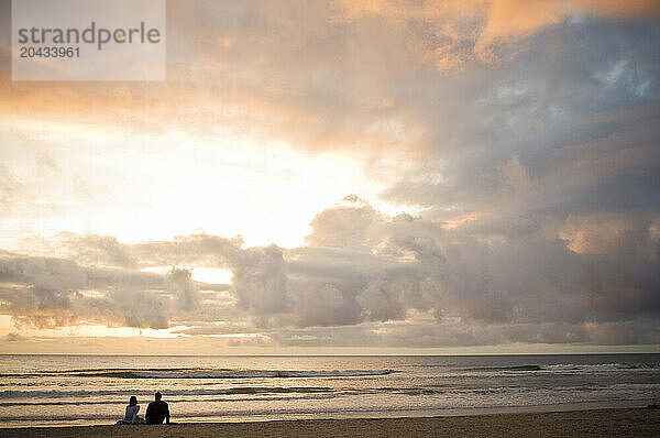 A couple sits on the beach watching the sunset