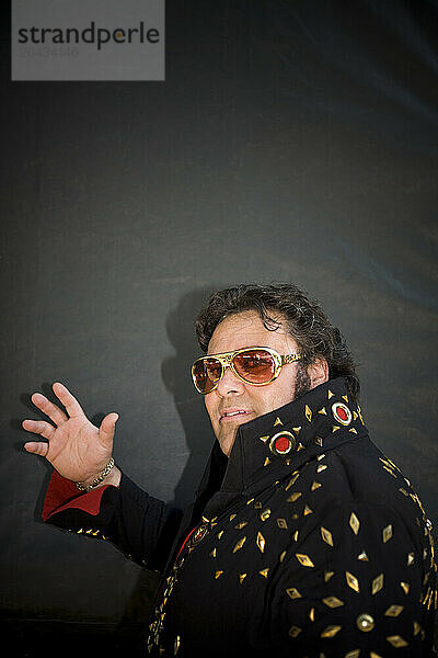 Elvis impersonator in a black costume with gold sunglasses on.