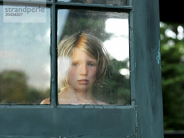 girl looks through window on a porch in maine