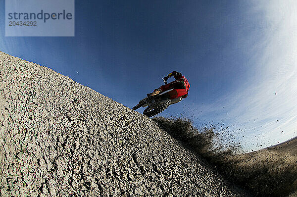 Dust and dirt fly as a young man climbs a steep hill on his dirt bike into a hard turn while motocross riding on the surreal dunes near Cameron  AZ.