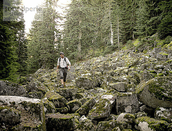 A middle aged male wearing a white shirt climbing down a landslide of rocks that is partially covered with moss.