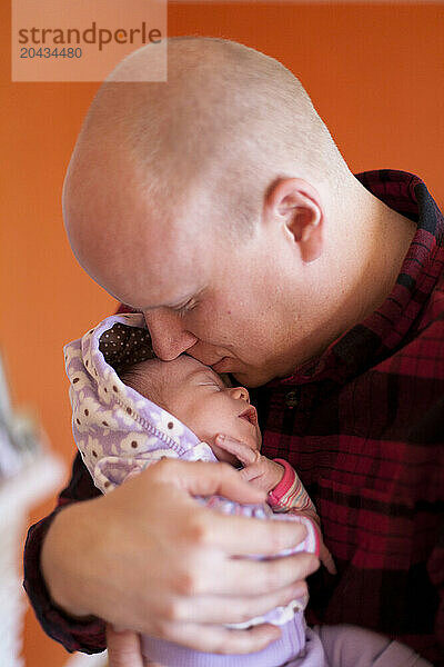 A father kisses his newborn baby as he holds her in his home.