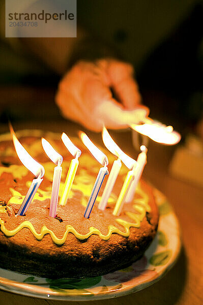 A blurred hand reaching to light candles on a birthday cake.