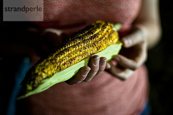 A close up photo of young woman in pink holding a piece of roast corn.