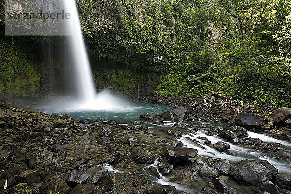 A group of tourists relax beneath a tropical waterfall