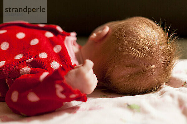 Close up of a newborn baby's red hair  as she lies on a green couch.