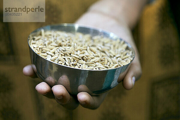 The hand of an Indian woman holding a ball of uncooked rice.