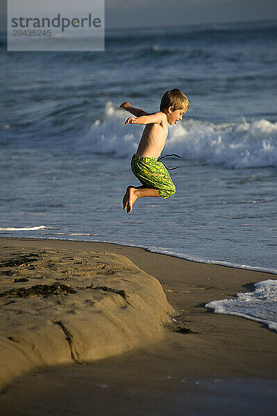 A young boy jumping at the beach.