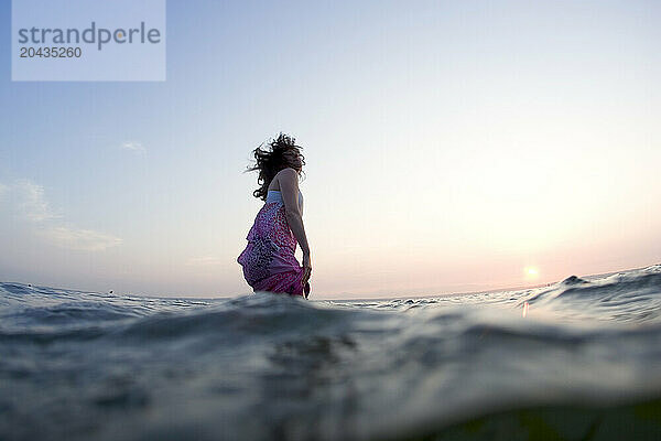 A girl happily walks into the Puget Sound at Golden Gardens park in Seattle during sunset.