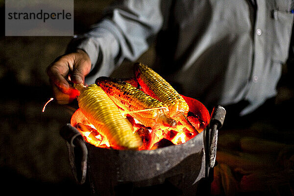 A middle aged man prepares roast-corn to sell at night on a beach.