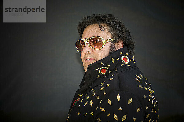 Elvis impersonator in a black costume with gold sunglasses on.