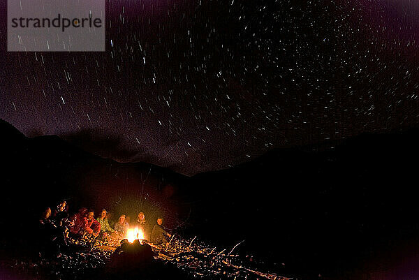 A group of people sit by a campfire under the stars during the first descent of the Salween River in Eastern Tibet.