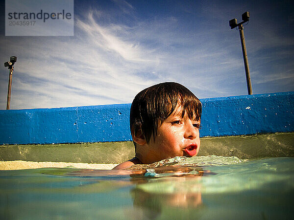 A young boy plays and swims in a swimming pool.