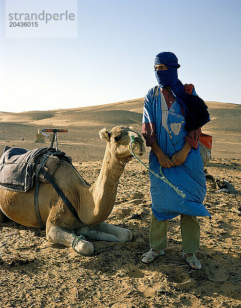 A Bedouin nomad rests with his camel before embarking on a journey across the Sahara Desert.