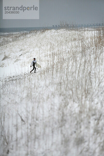 A surfer trudges through the winter snow on Wrightsville Beach