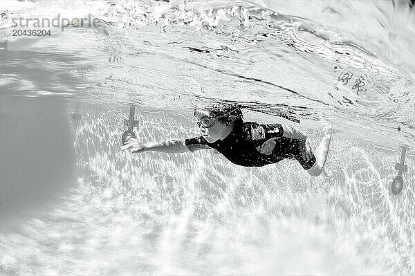 A young boy learns to swims underwater in a pool.